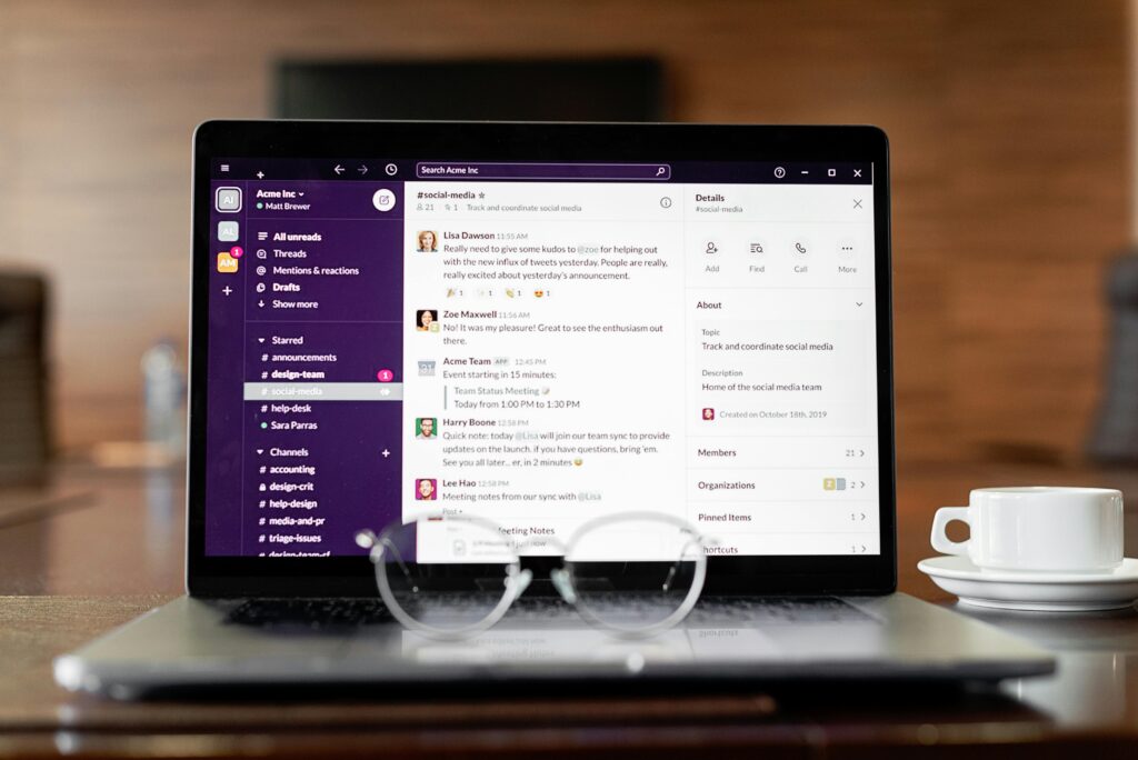 Laptop displaying a messaging app, with eyeglasses and coffee cup on a wooden table.
